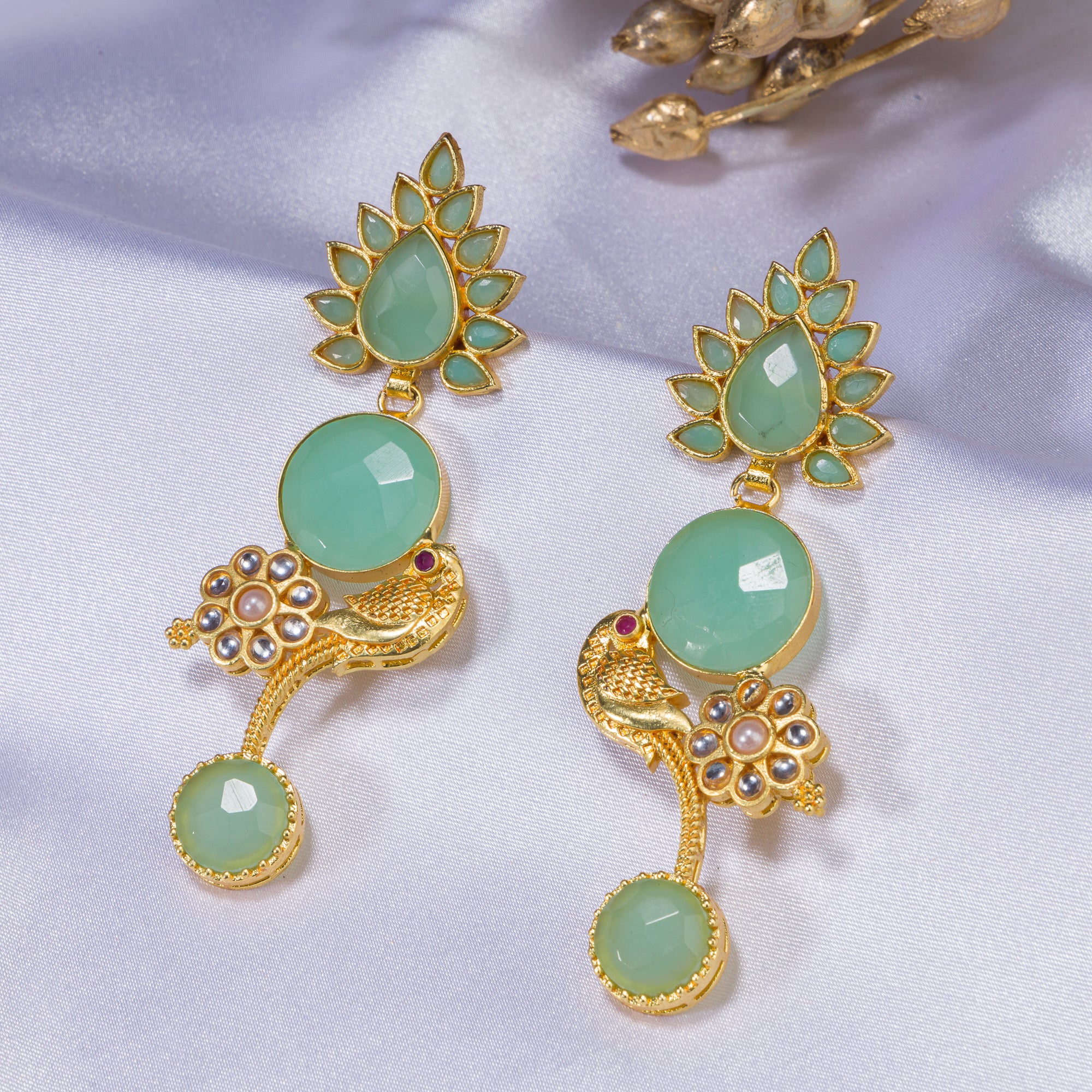 "Gold-tone dangler earrings with light green accents blend warmth and freshness for a chic, eye-catching festival look."