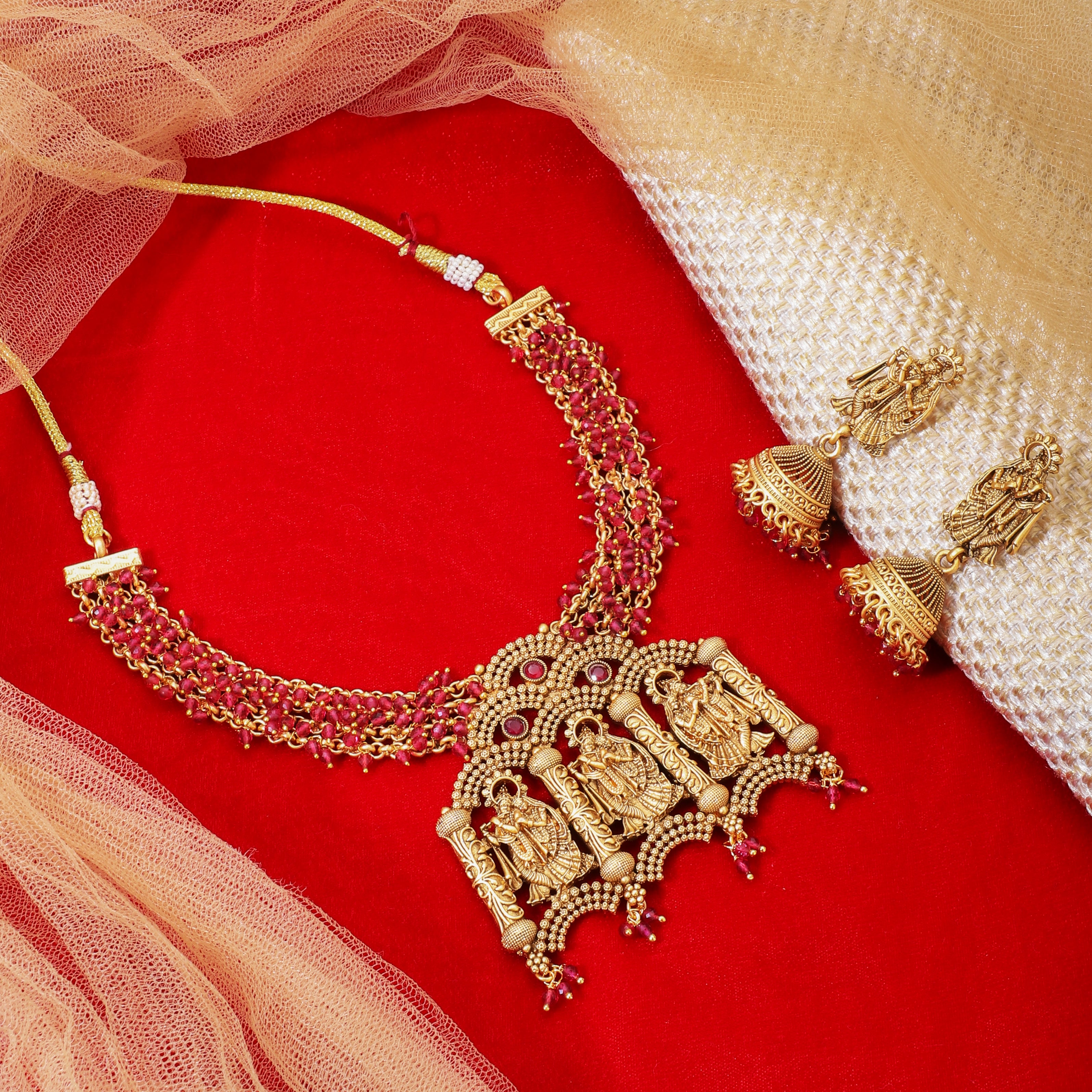 Radha Krishna temple necklace set with red pearls, showcasing intricate gold-tone craftsmanship.