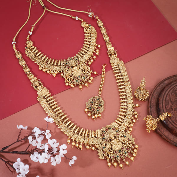 "Goldtone Laxmi Maa crafted long necklace set with matching earrings and Maang Tikka for festive elegance."