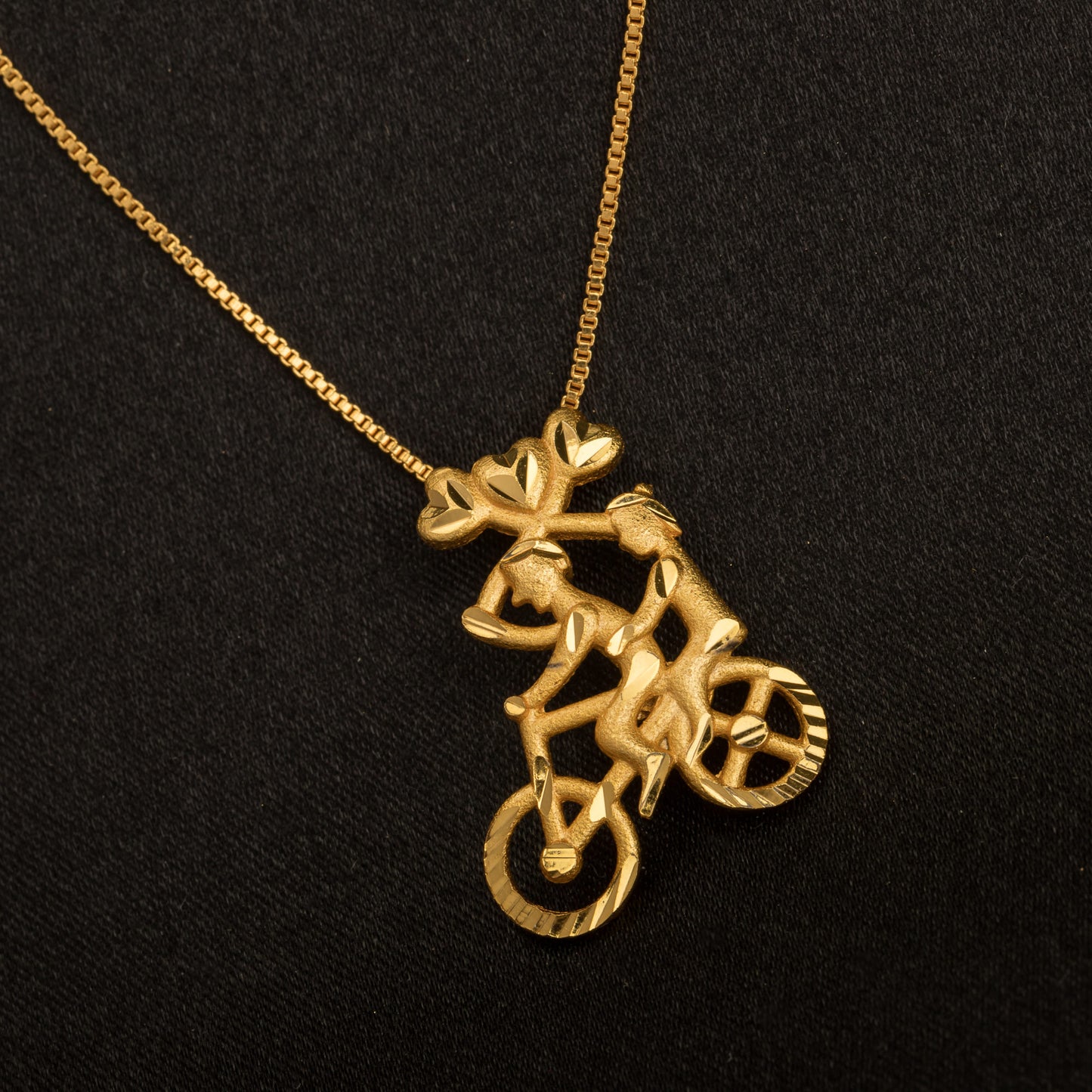 GOLD-TONE PENDANT FEATURING A BOY RIDING A BICYCLE.