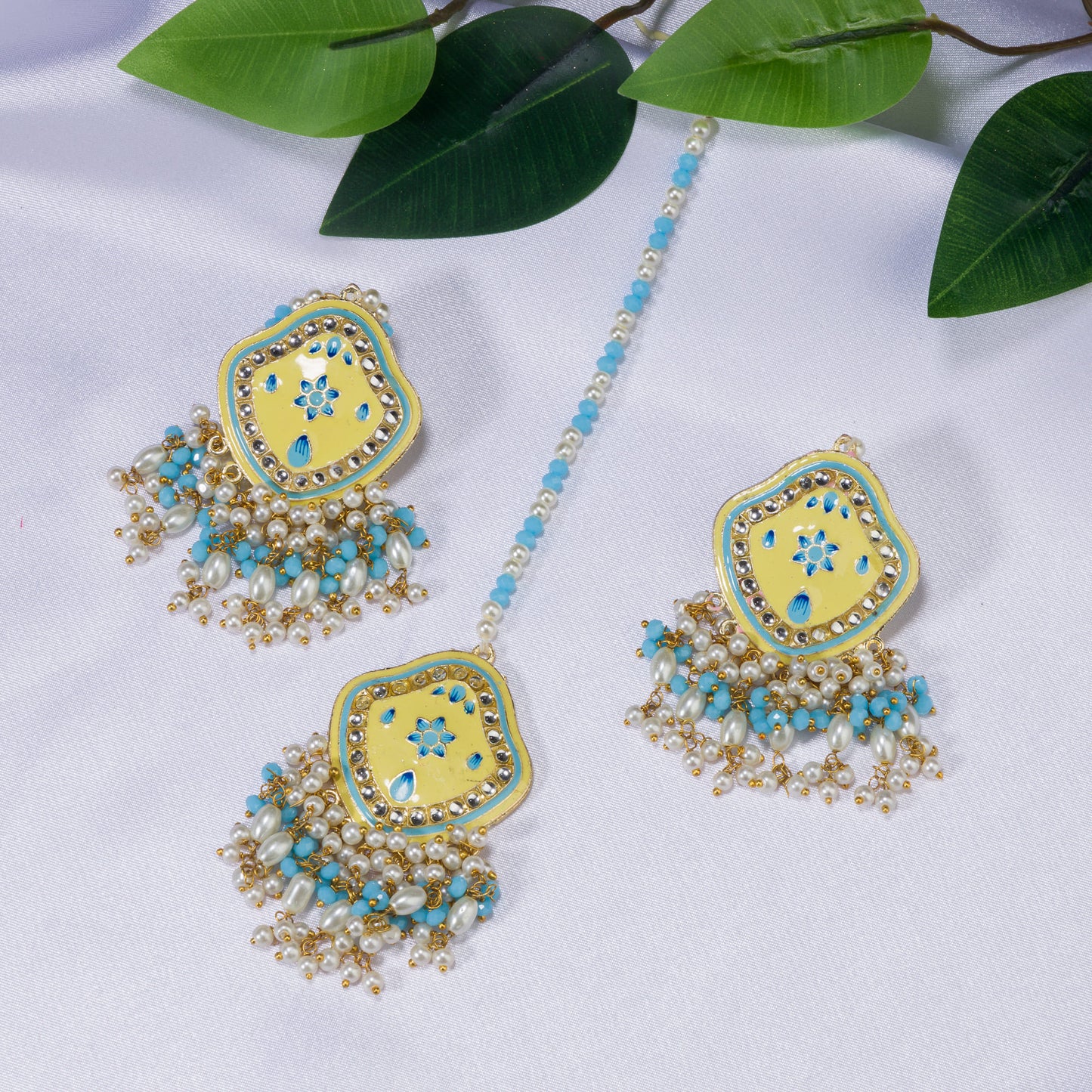 "WHEAT-COLORED EARRINGS AND MAANGTIKA, ADORNED WITH AQUA AND WHITE PEARL BEADS, OFFER A GRACEFUL BLEND OF SUBTLE ELEGANCE AND VIBRANT CHARM."