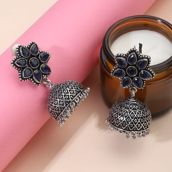 ADD A TOUCH OF ELEGANCE WITH THESE BLUE STONES STUDDED OXIDIZED JHUMKAS. FEATURING A BEAUTIFUL FLOWER DESIGN, T