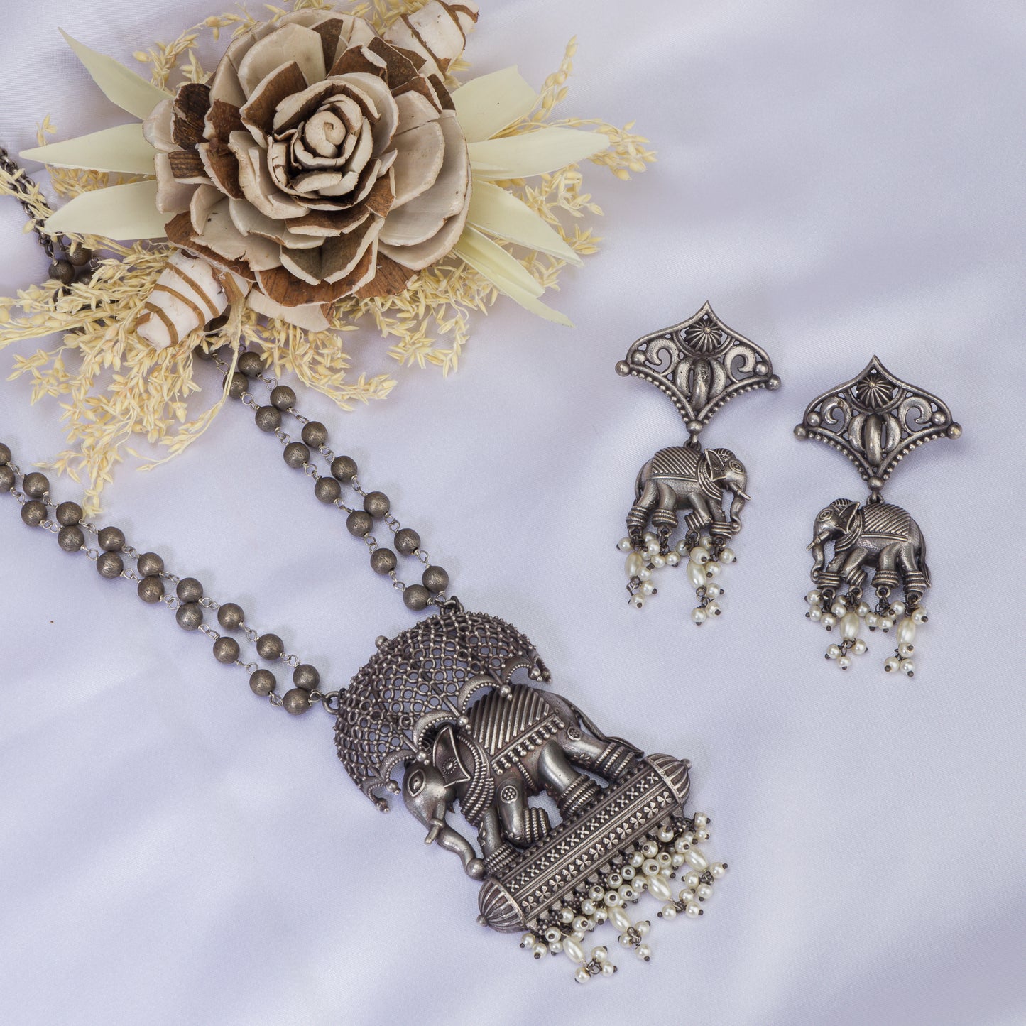 AN OXIDIZED LONG NECKLACE WITH UMBRELLA, ELEPHANT, AND WHITE PEARLS EXUDES VINTAGE CHARM.