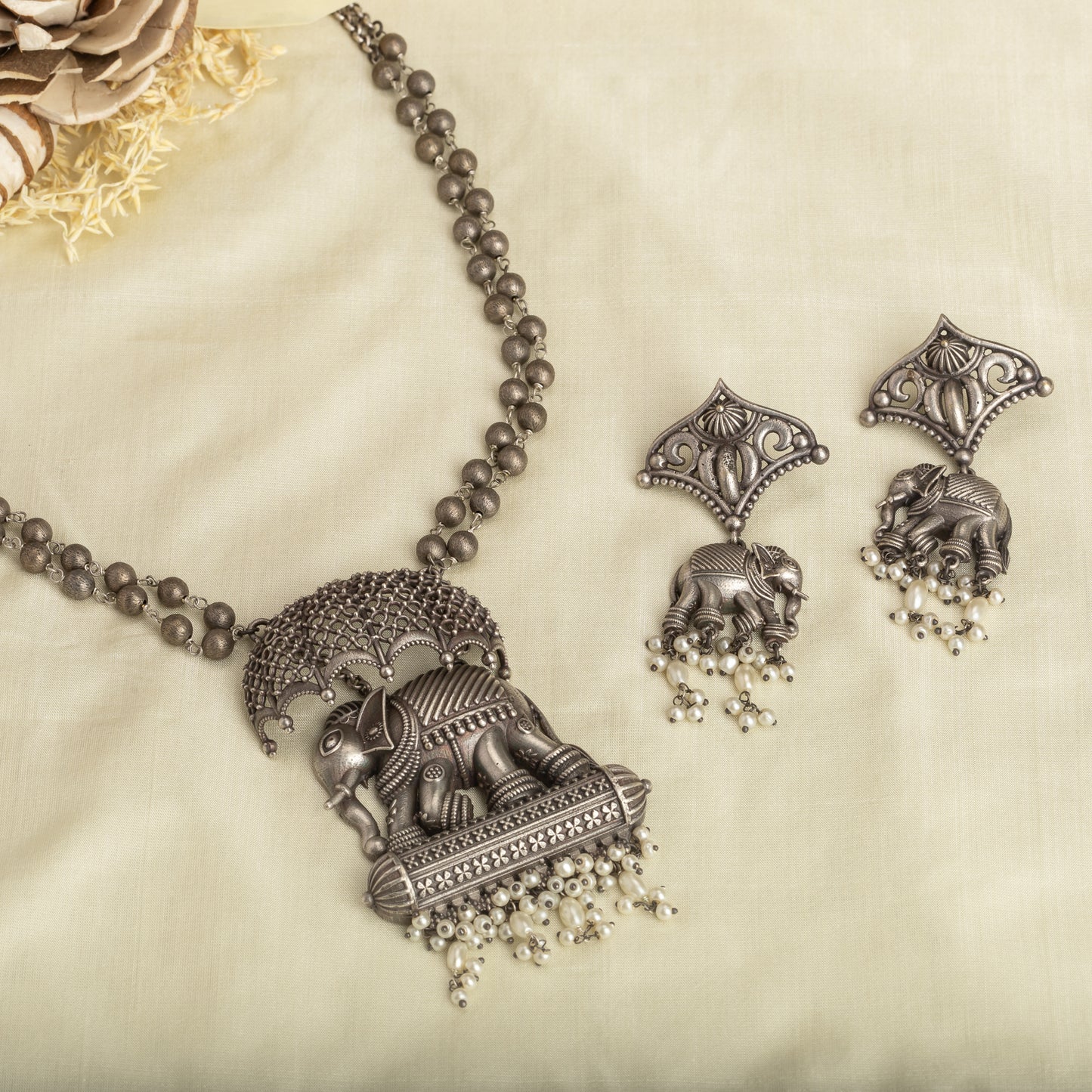 AN OXIDIZED LONG NECKLACE WITH UMBRELLA, ELEPHANT, AND WHITE PEARLS EXUDES VINTAGE CHARM.