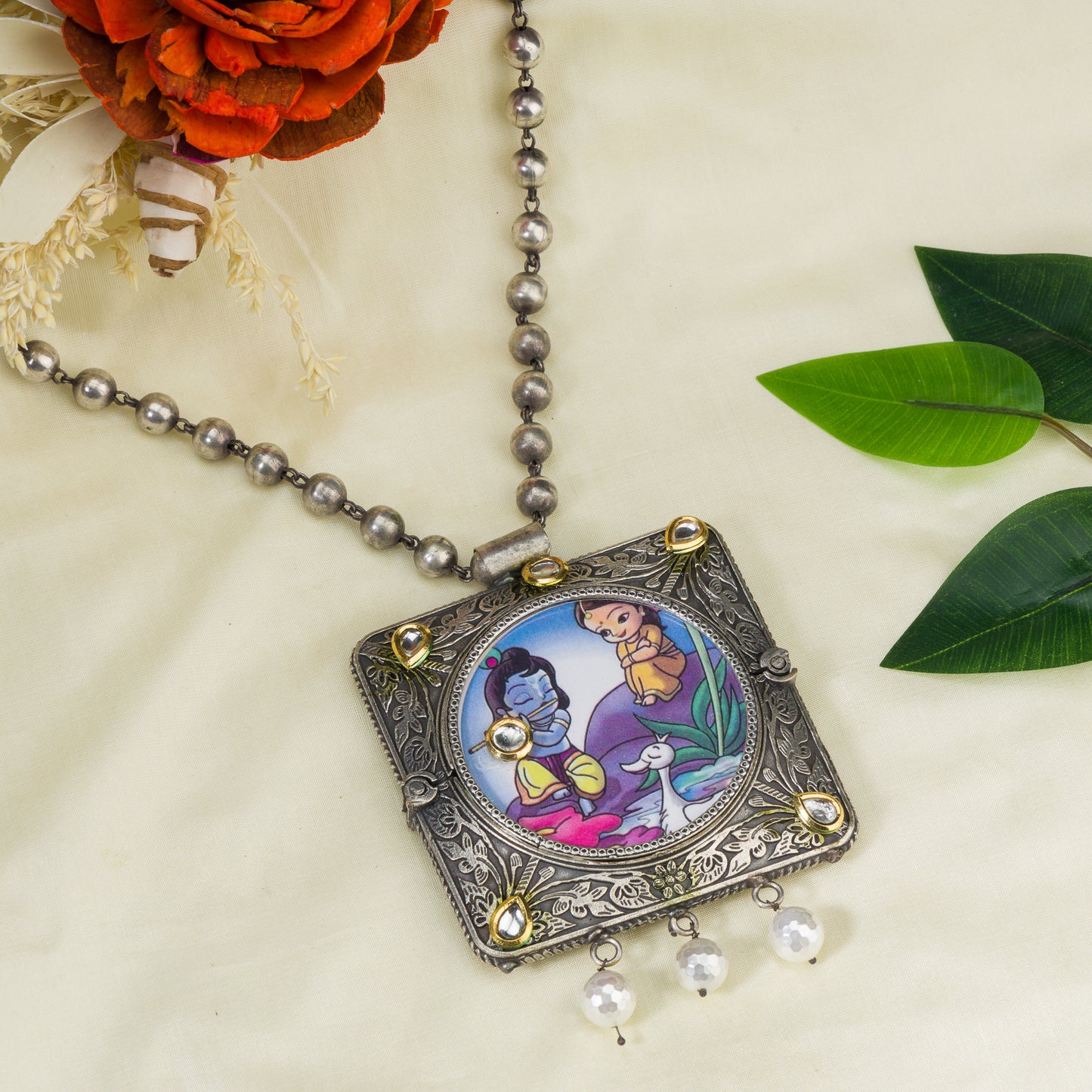 A LONG OXIDIZED NECKLACE WITH A RADHA KRISHNA IMAGE ADDS SPIRITUAL CHARM.