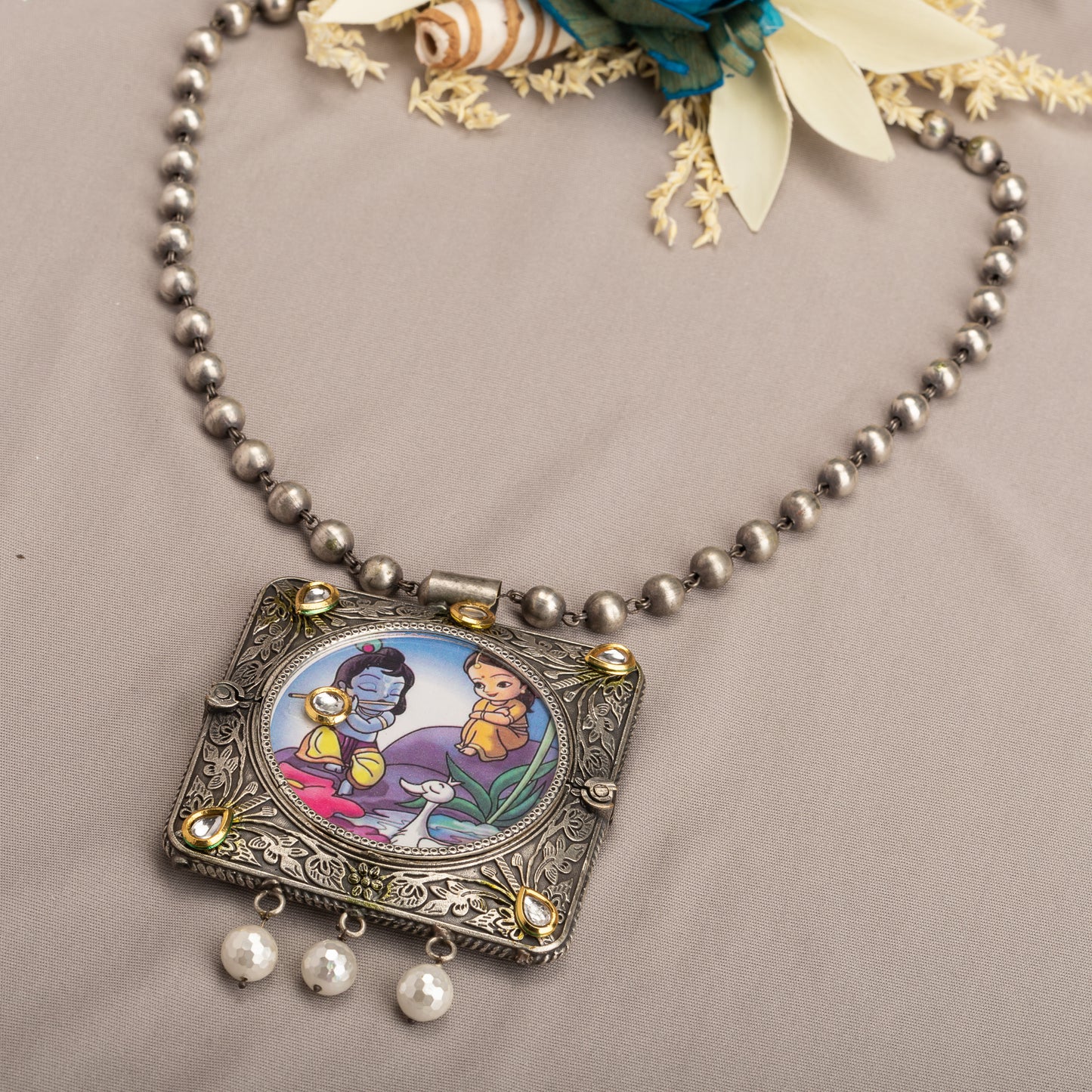 A LONG OXIDIZED NECKLACE WITH A RADHA KRISHNA IMAGE ADDS SPIRITUAL CHARM.