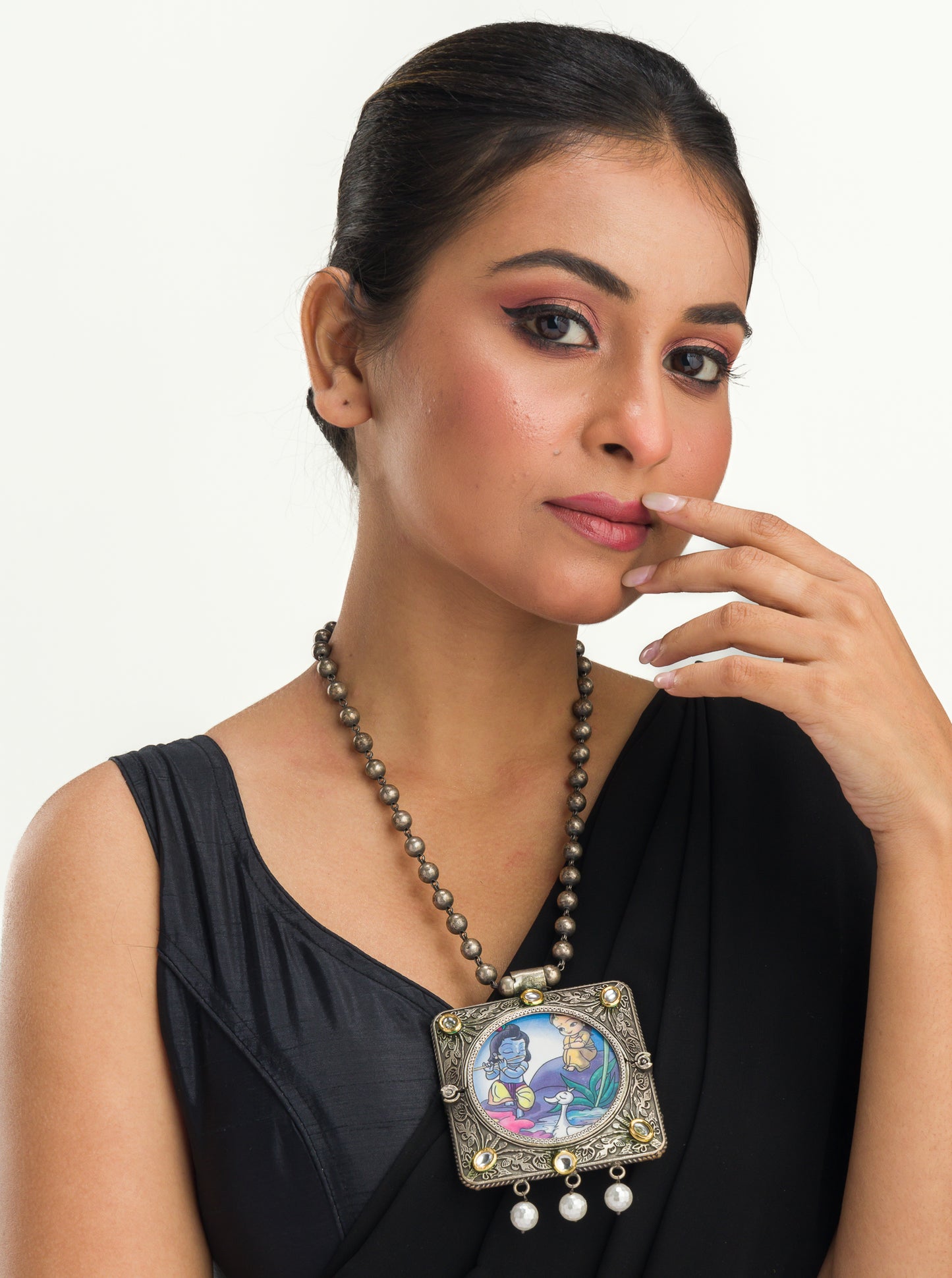 A LONG OXIDIZED NECKLACE WITH A RADHA KRISHNA IMAGE ADDS SPIRITUAL CHARM.