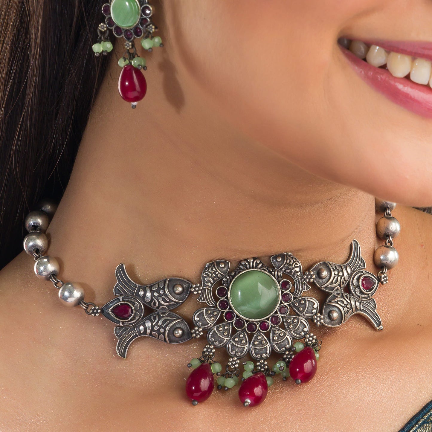 A FISH NECKLACE WITH LIGHT GREEN STONES AND MAROON KUNDAN BLENDS UNIQUE CHARM WITH RICH COLORS.