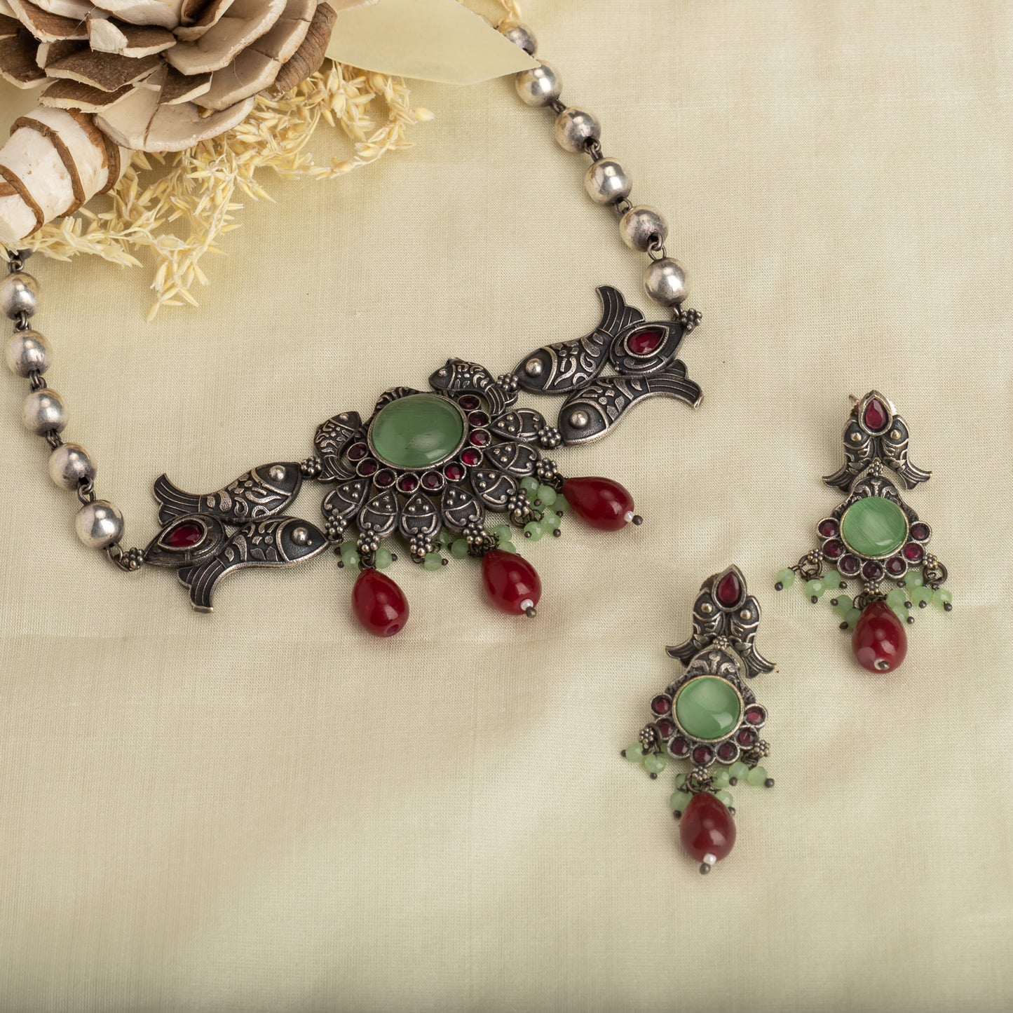 A FISH NECKLACE WITH LIGHT GREEN STONES AND MAROON KUNDAN BLENDS UNIQUE CHARM WITH RICH COLORS.