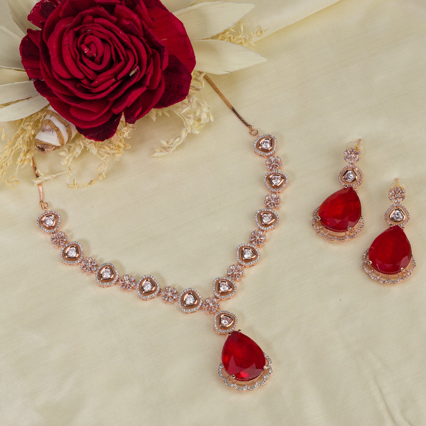 THIS ROSE GOLD POLISHED NECKLACE SET SHOWCASES A STRIKING PENDANT WITH LARGE RED STONES, BEAUTIFULLY ACCENTED BY ZIRCON STUDS.