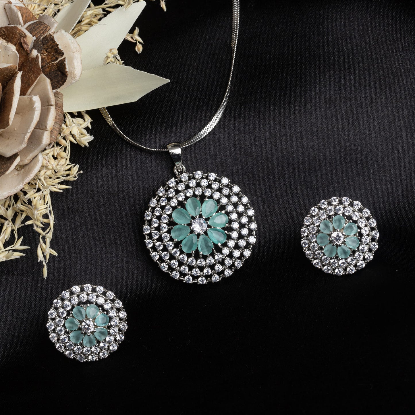 THIS PENDANT SET FEATURES A FLORAL DESIGN ADORNED WITH TURQUOISE AND WHITE ZIRCON STONES , PAIRED WITH MATCHING EARRINGS, .